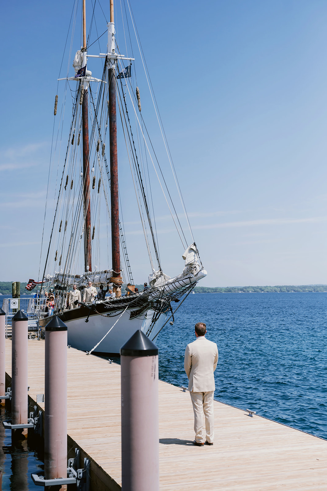 Man in a suit with his back to the camera looking at the sailboat on the dock 