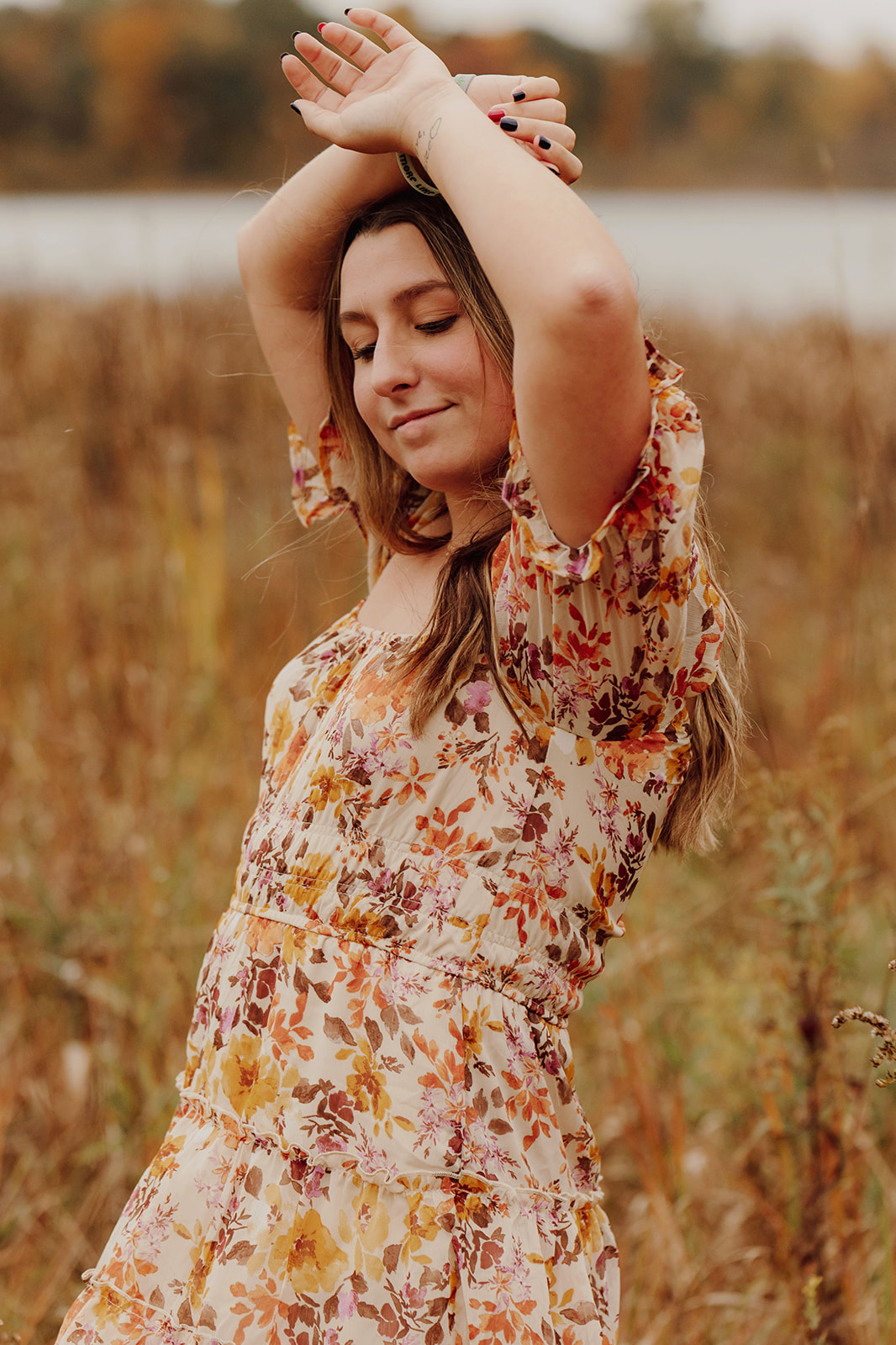 Senior picture outfit ideas: Stunning senior wearing a floral dress and raising her hands over her head as she smiles during the shoot in the middle of a field.