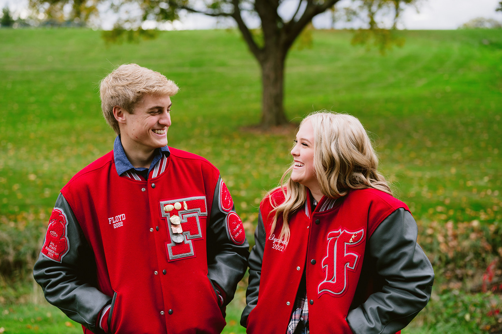 Senior Picture Outfit Ideas: Guy and girl looking and smiling at each other while wearing matching Letterman jackets.