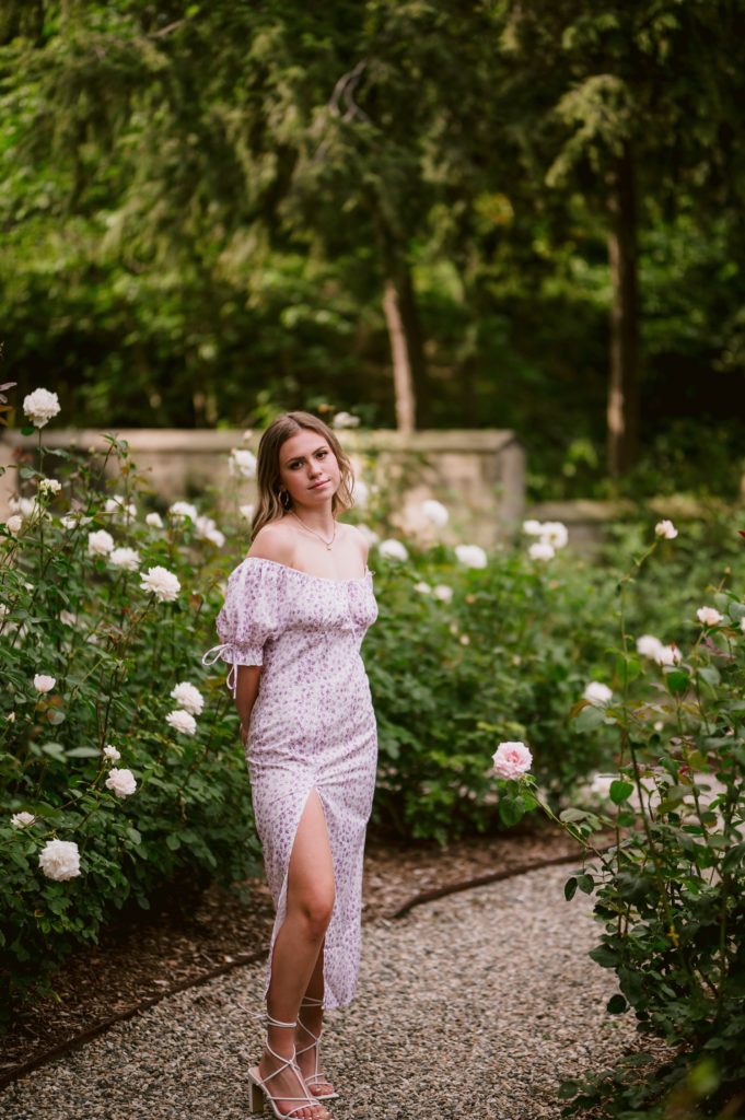 Senior Picture Outfit Ideas for Girls: Stunning girl posing in her gorgeous dress next to lovely flowers for their senior photoshoot.