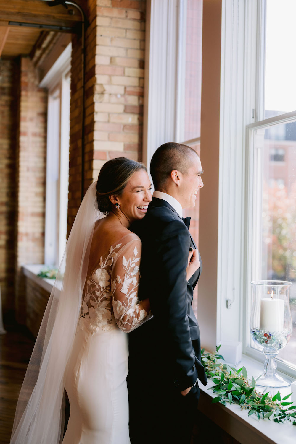 Bride smiles as she wraps her arms around the groom looking out the window at the Loft at Luna, taken by Mary Shelton Media