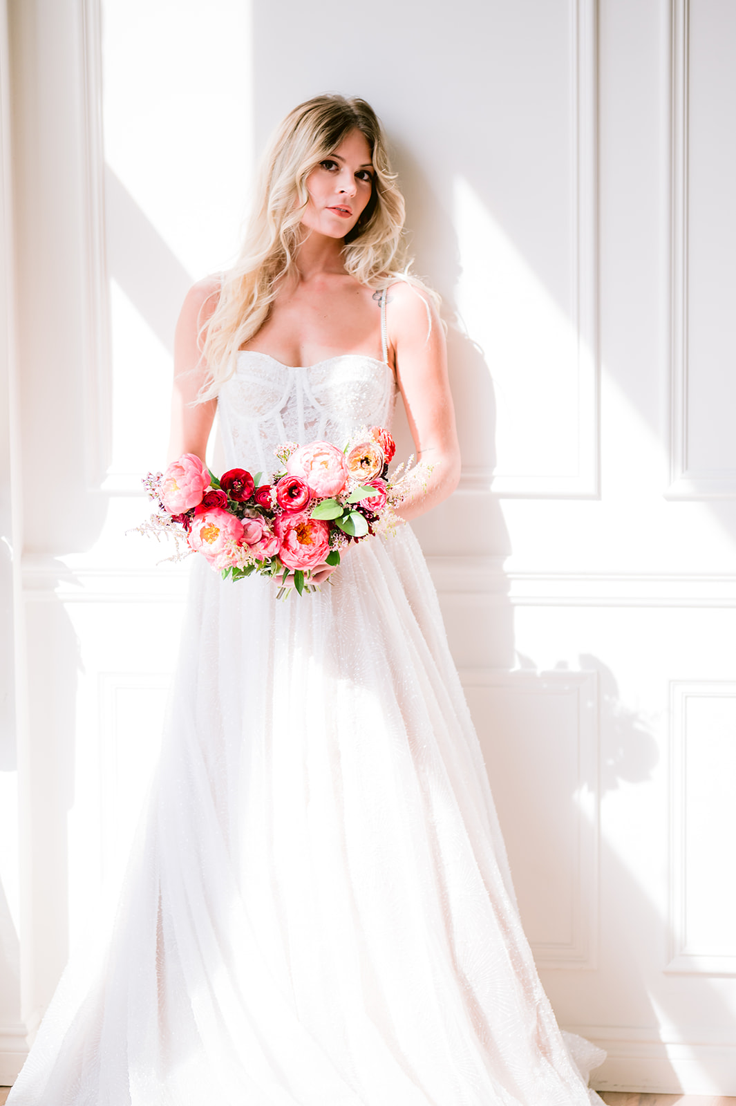 Gorgeous bride leaning against white wall as she holds her vibrant bouquet, captured by Michigan wedding photographer Mary Shelton